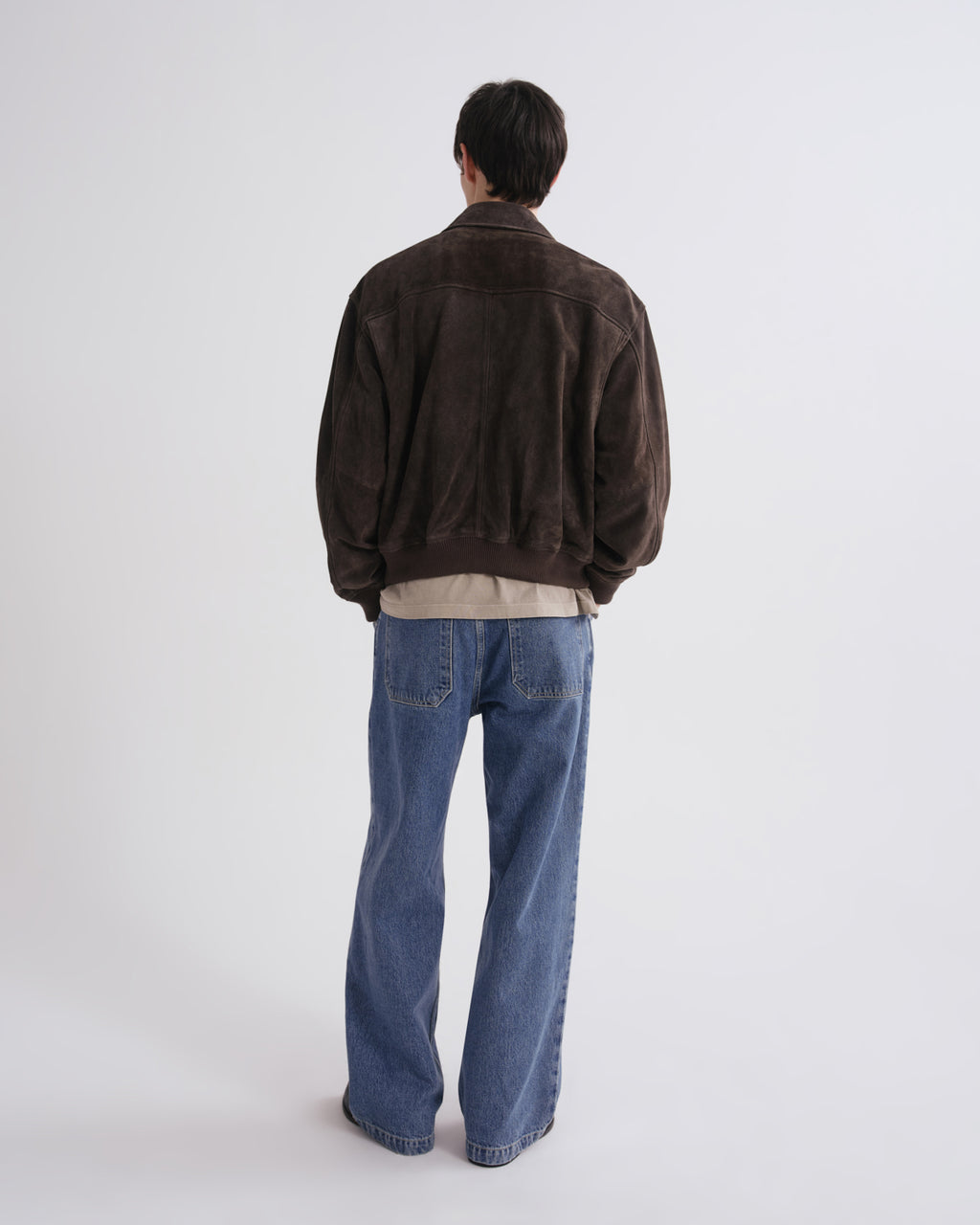 Person wearing a brown jacket and blue jeans on a grey background