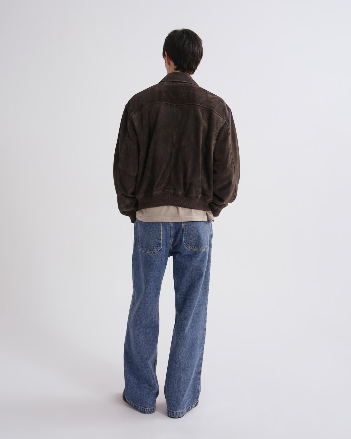 Person wearing a brown jacket and blue jeans on a grey background