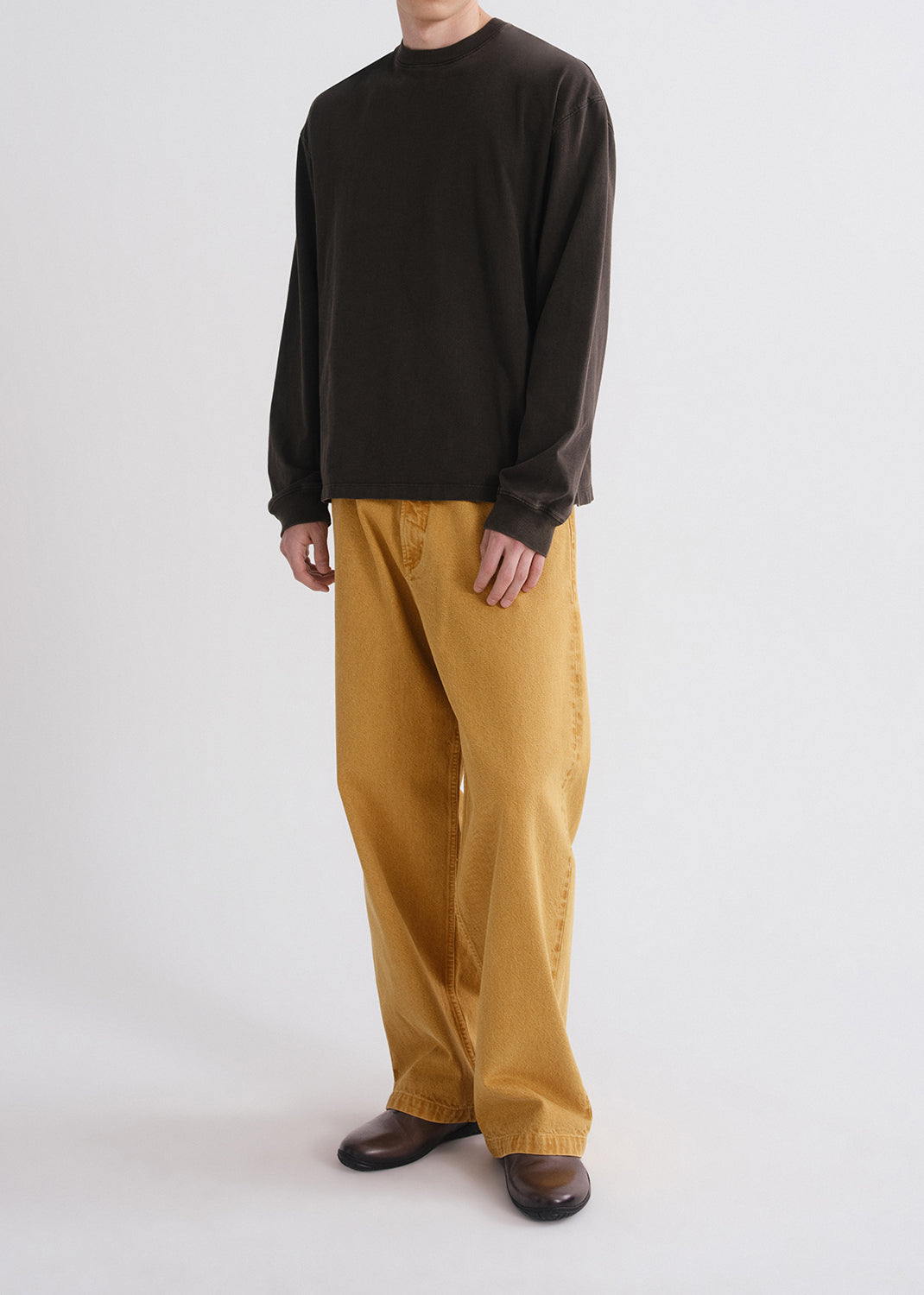 Person wearing a black long-sleeve shirt and mustard yellow pants on a grey background