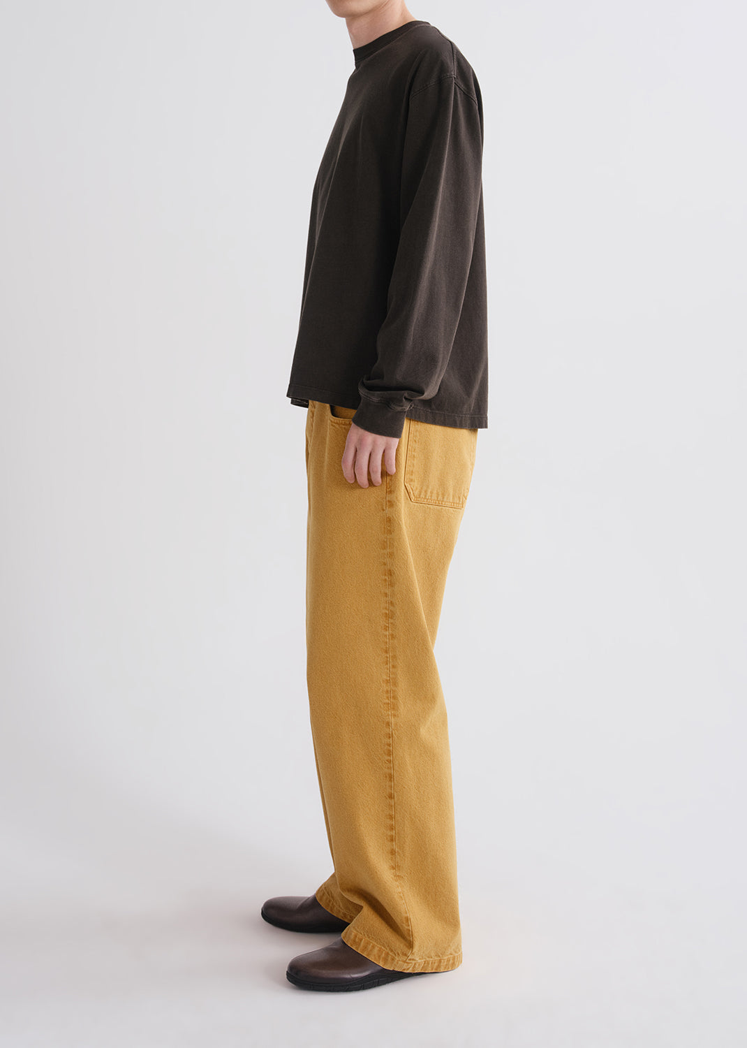 Side view of person wearing a black long-sleeve shirt and mustard yellow pants on a grey background