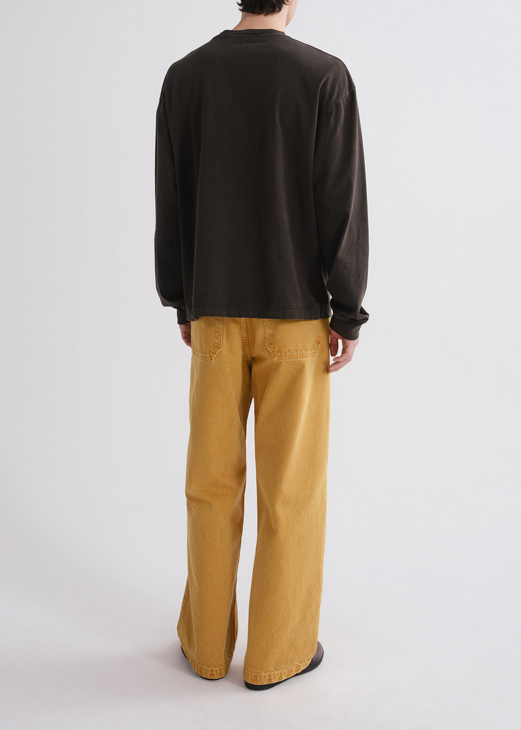 Person wearing a black long-sleeve shirt and mustard yellow pants on a grey background