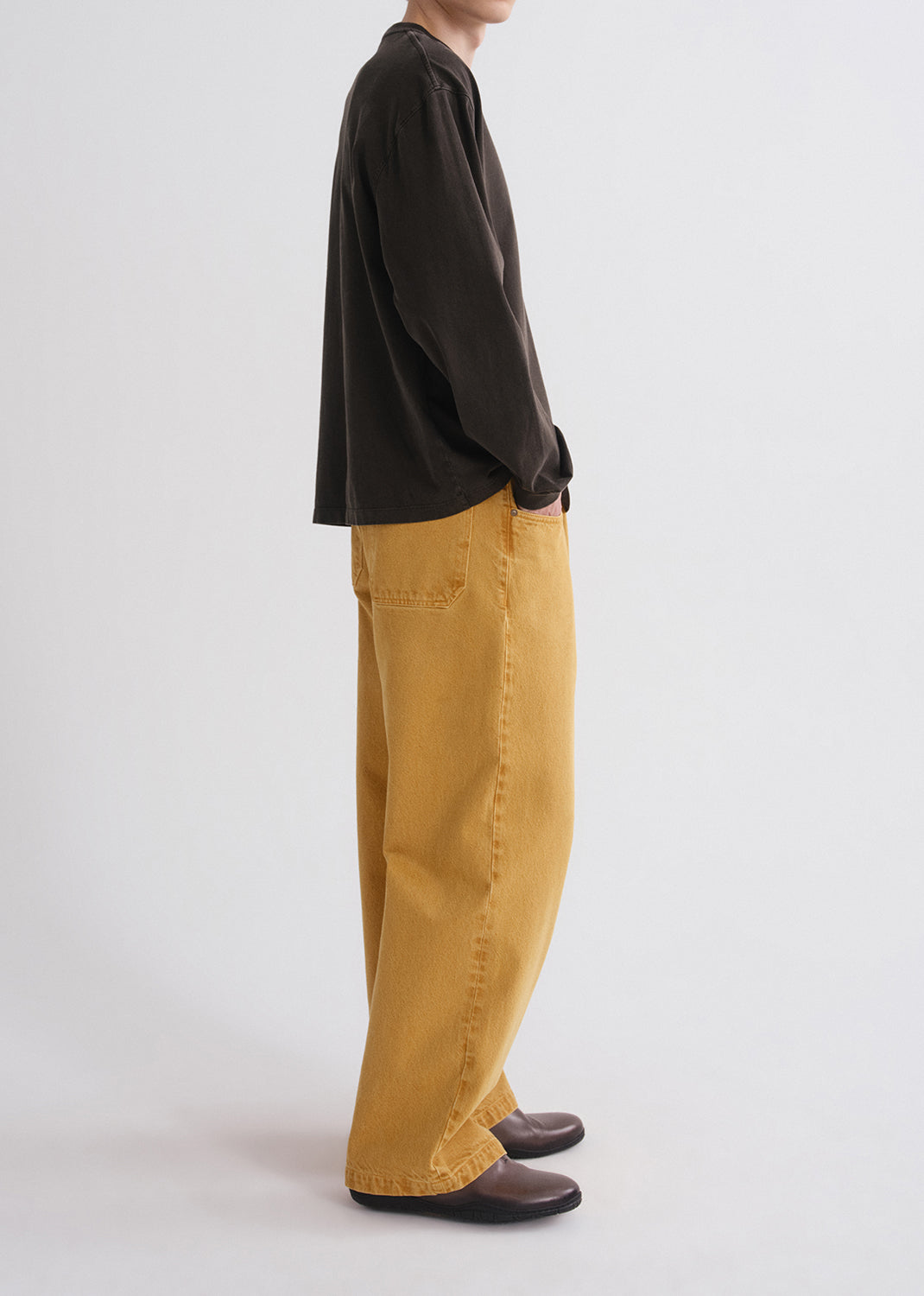 Side view of person wearing a black long-sleeve shirt and mustard yellow pants on a grey background