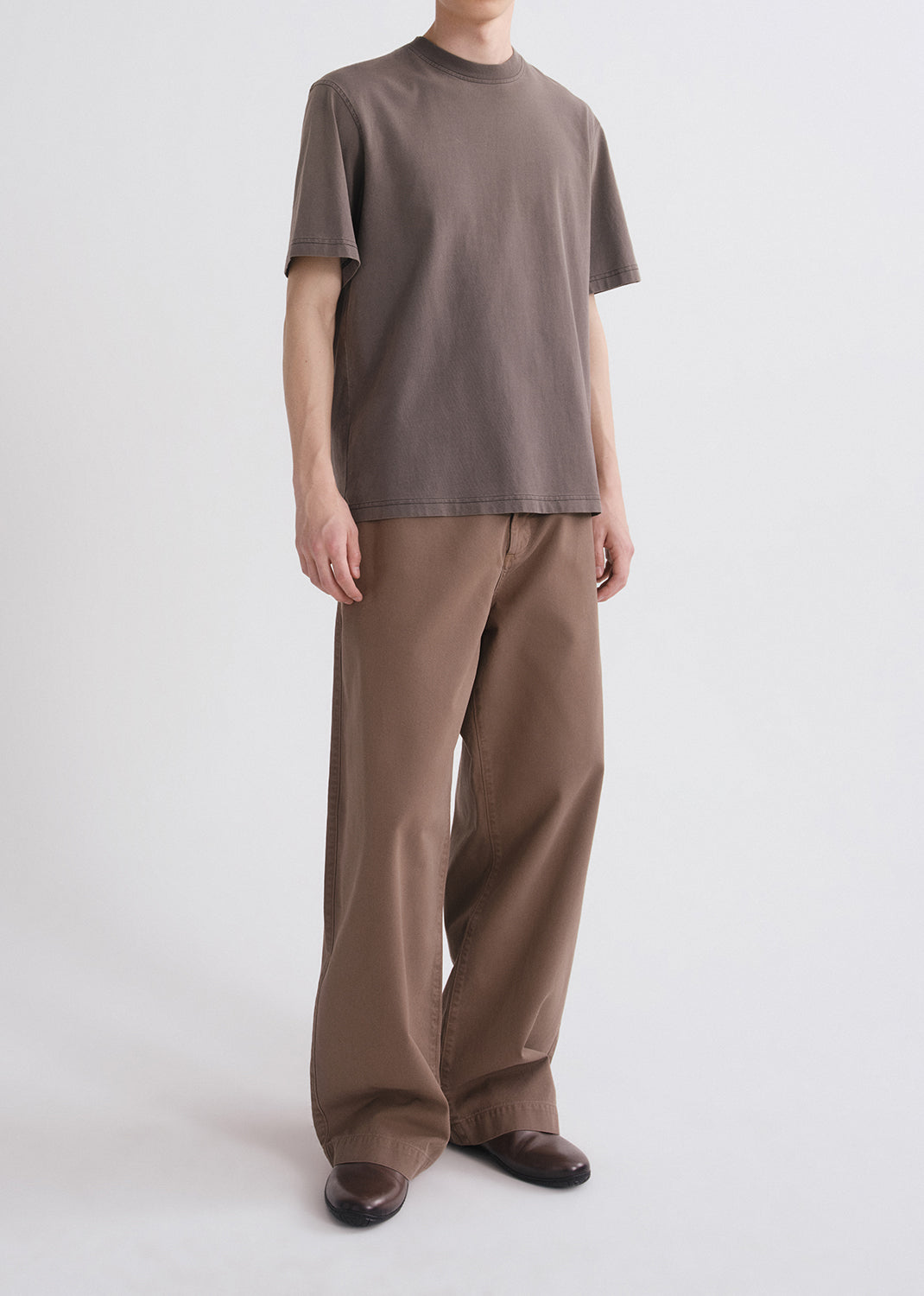 Side shot of person wearing a brown shirt and brown pants on a grey background