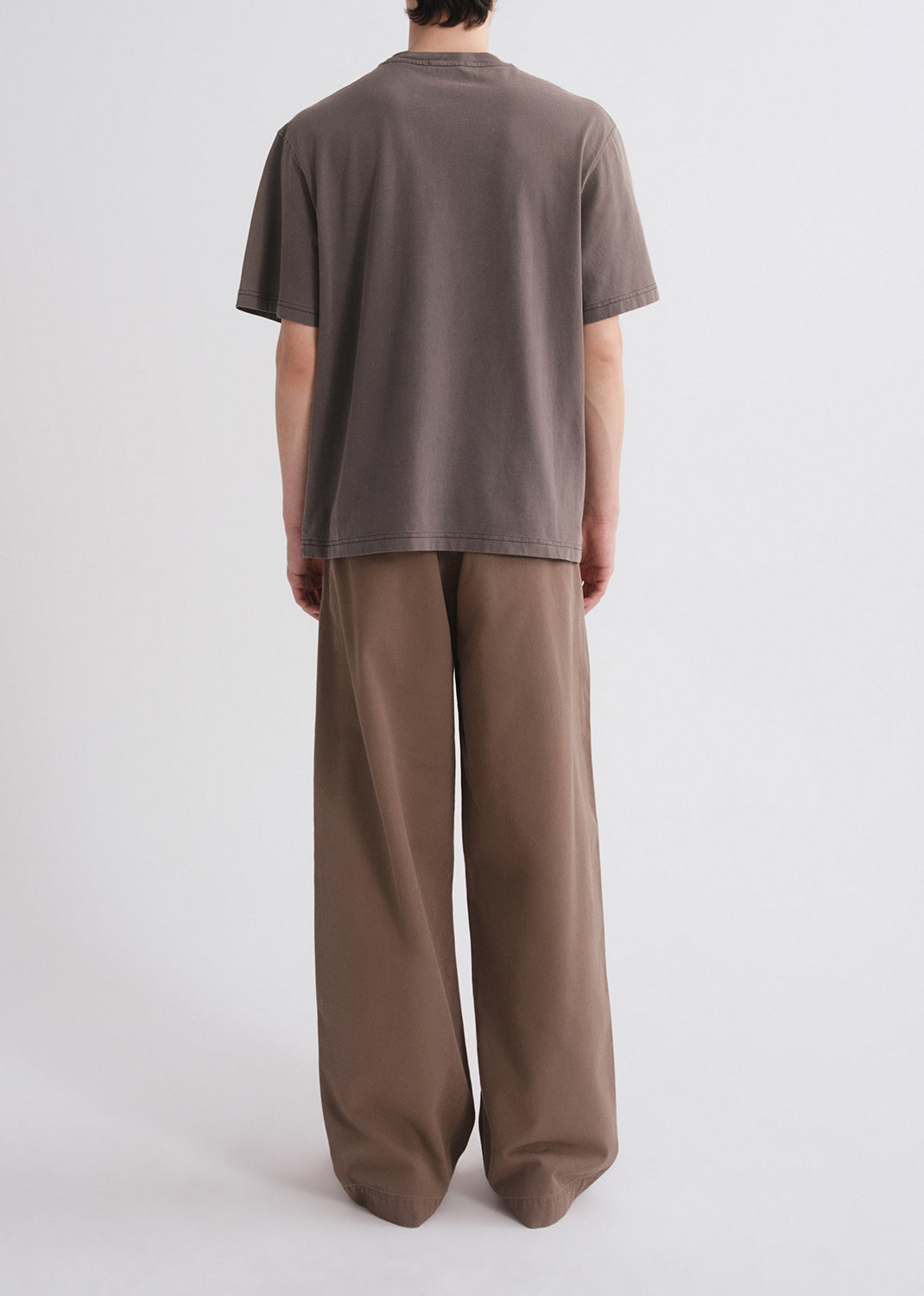 Back shot of person wearing a brown shirt and brown pants on a grey background