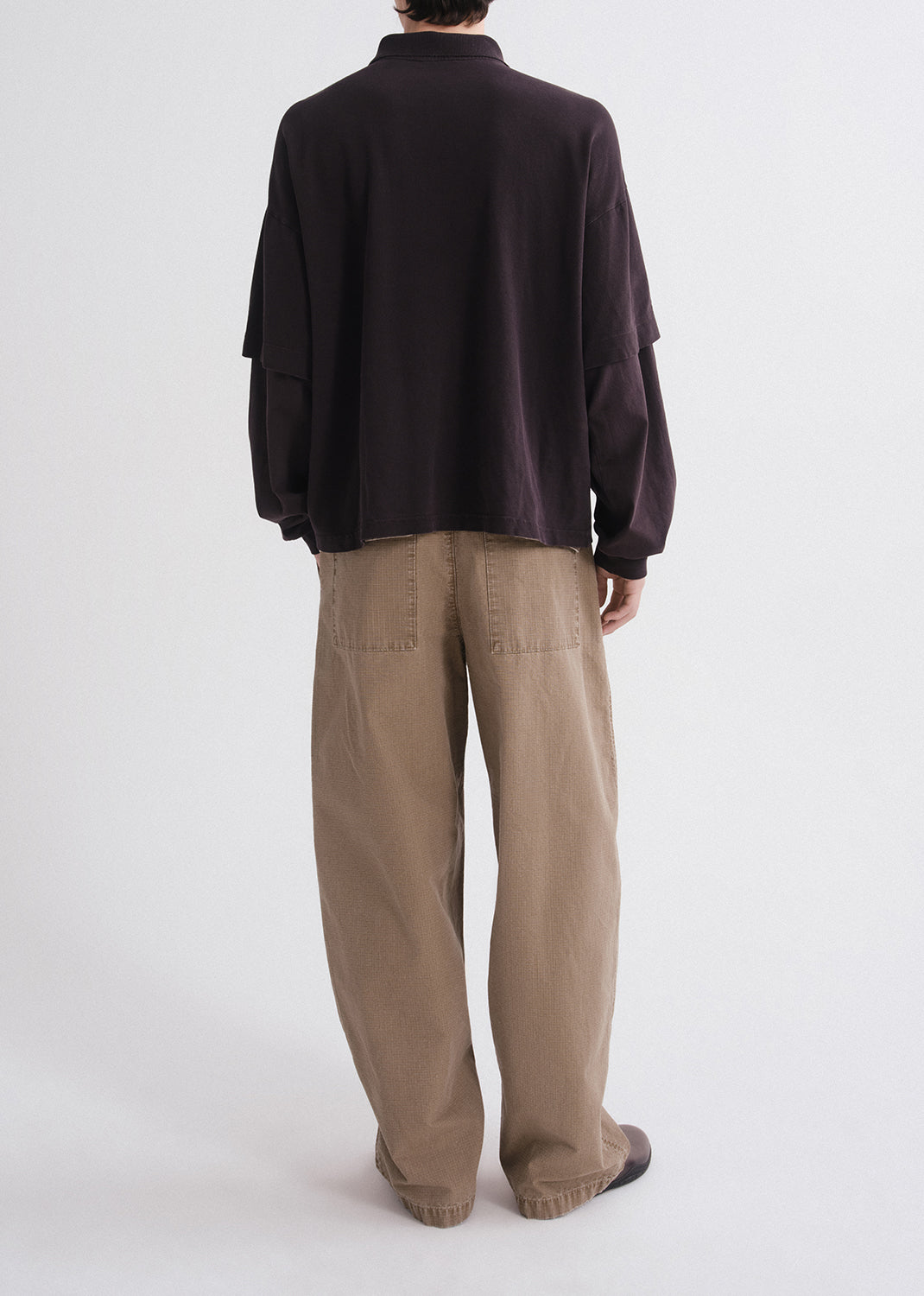 Person wearing a dark brown shirt and beige pants on a grey background