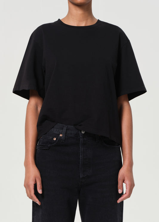 Person wearing a black oversized t-shirt and black pants on a light gray background