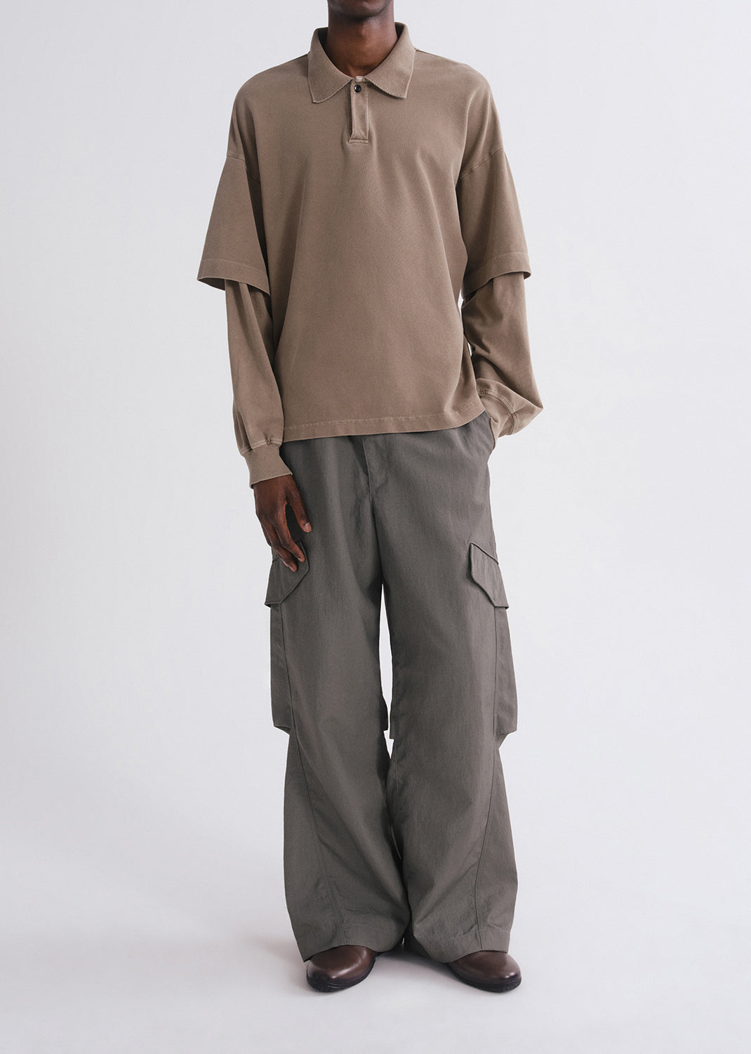 Person wearing brown long sleeve and green pants on a grey background