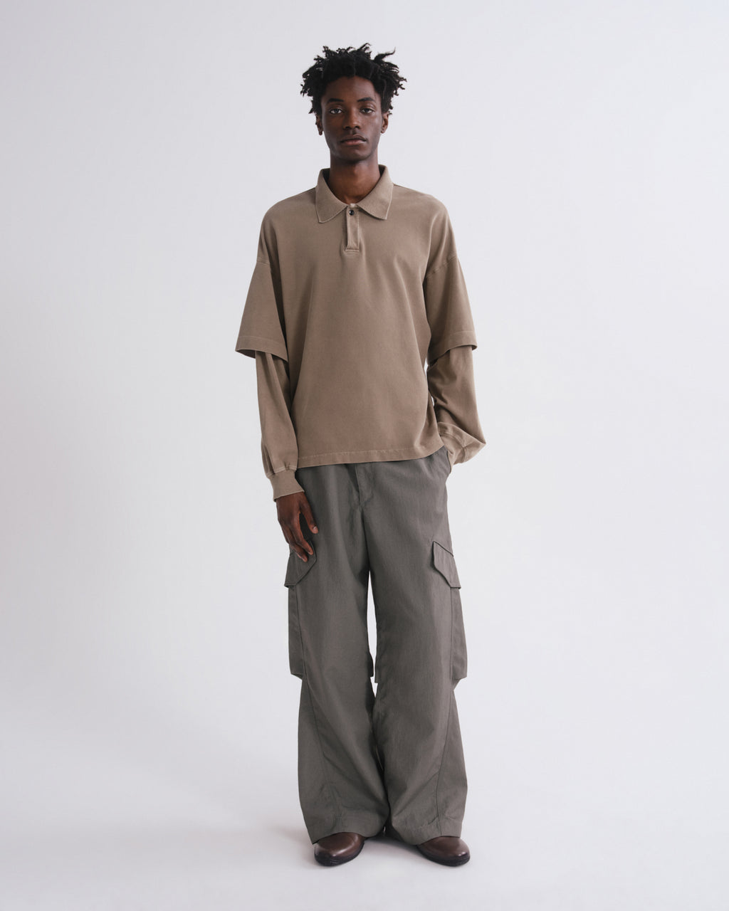 A model stands against a light gray studio background wearing a taupe long-sleeve polo shirt and wide-leg gray cargo pants.