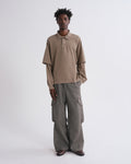 A model stands against a light gray studio background wearing a taupe long-sleeve polo shirt and wide-leg gray cargo pants.