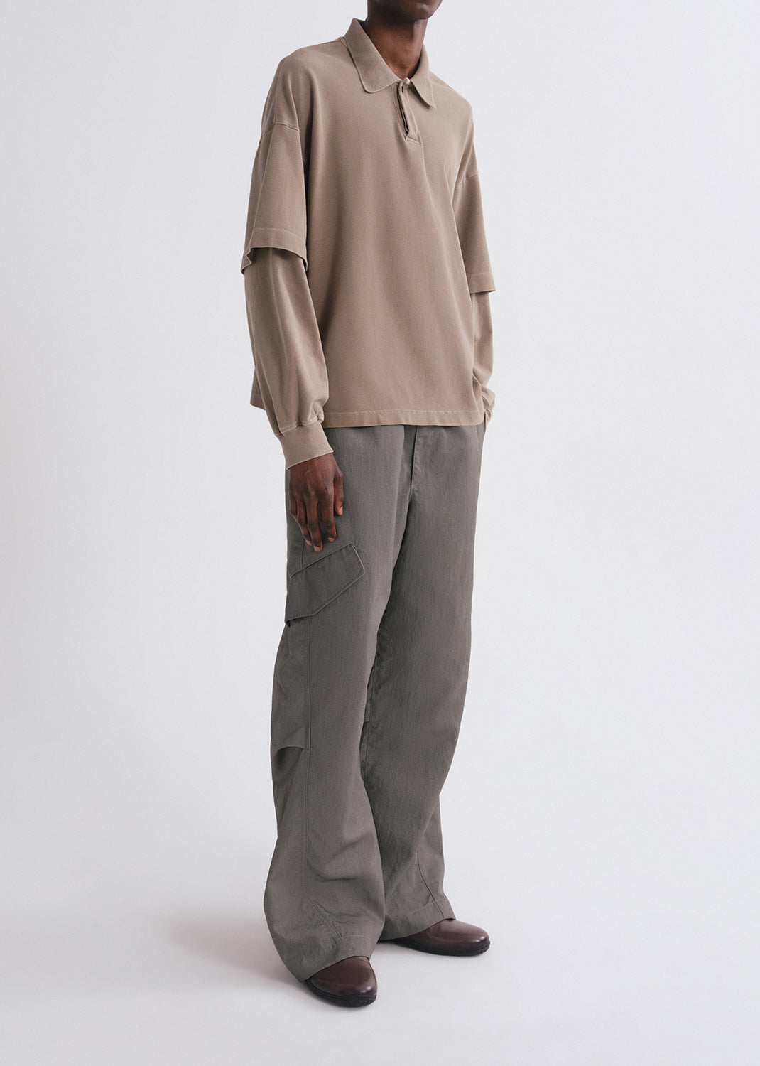 Side shot of person wearing brown long sleeve and green pants on a grey background