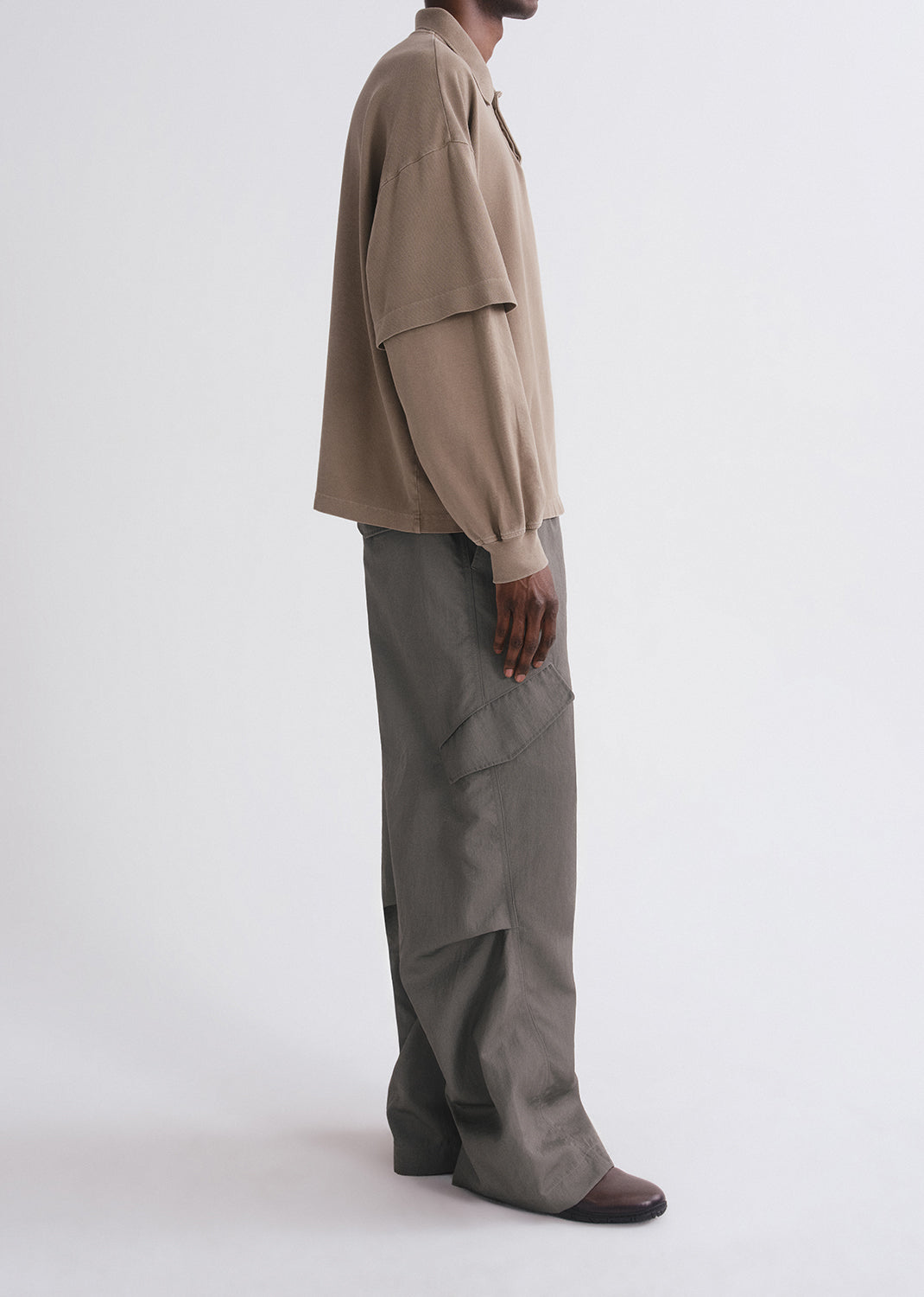 Side shot of person wearing brown long sleeve and green pants on a grey background