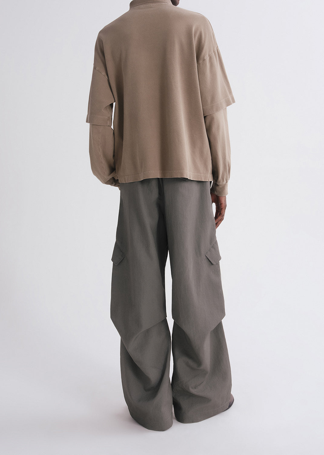 Back shot of person wearing brown long sleeve and green pants on a grey background