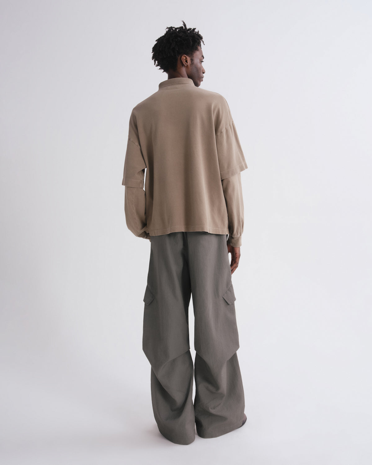A model shown from the back wearing a beige long-sleeve cropped shirt and wide-leg taupe cargo pants against a plain light gray studio background.