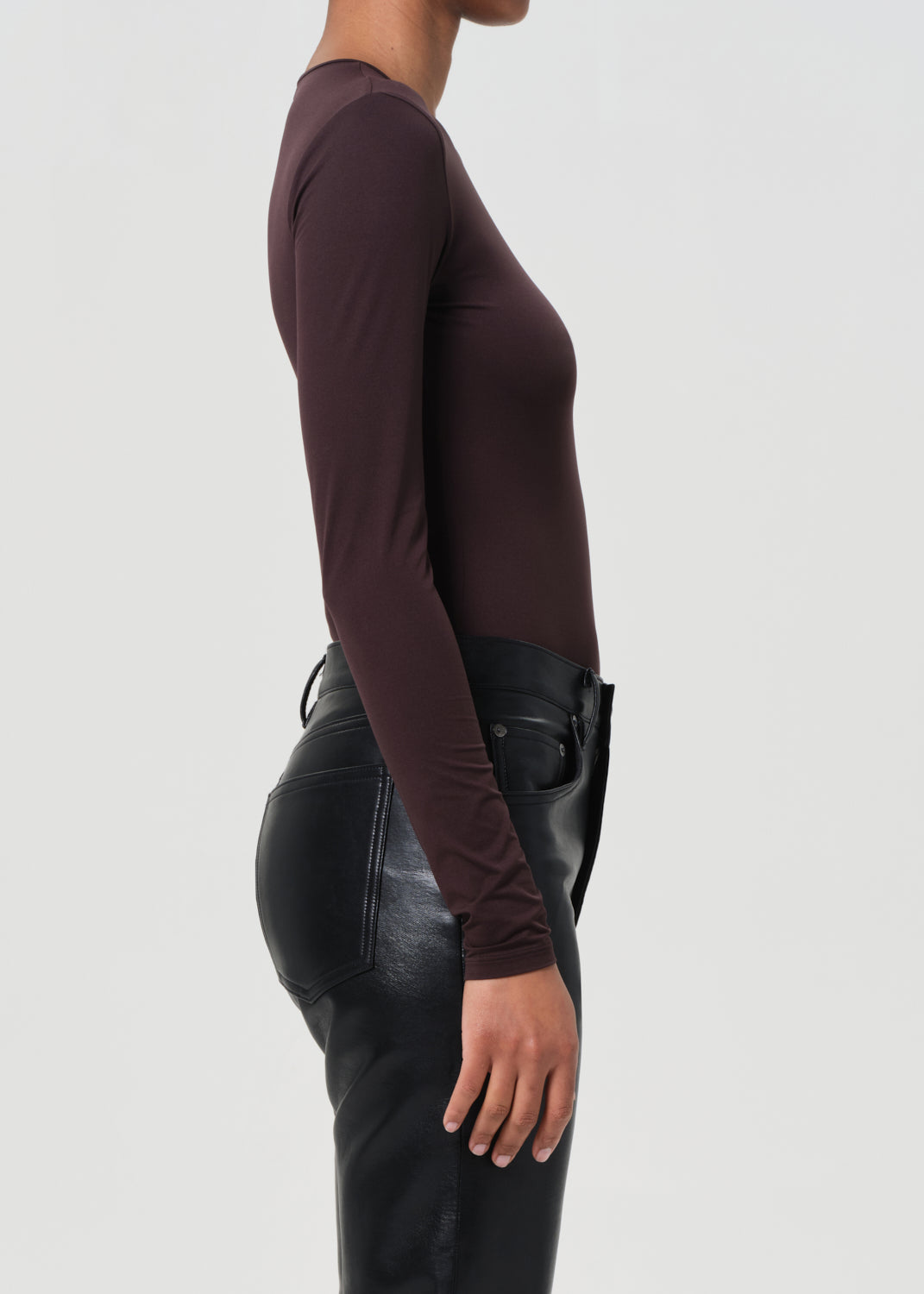 Person wearing a brown long-sleeve top and black leather pants on a white background
