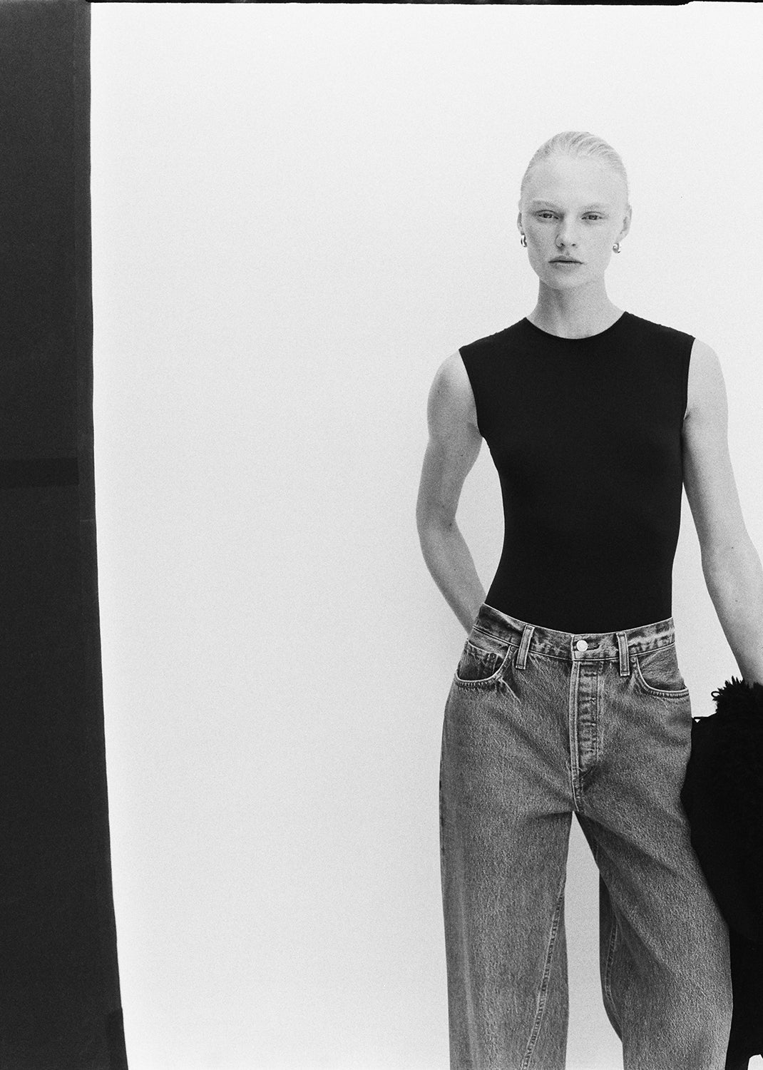 Person wearing a black sleeveless top and jeans against a white background