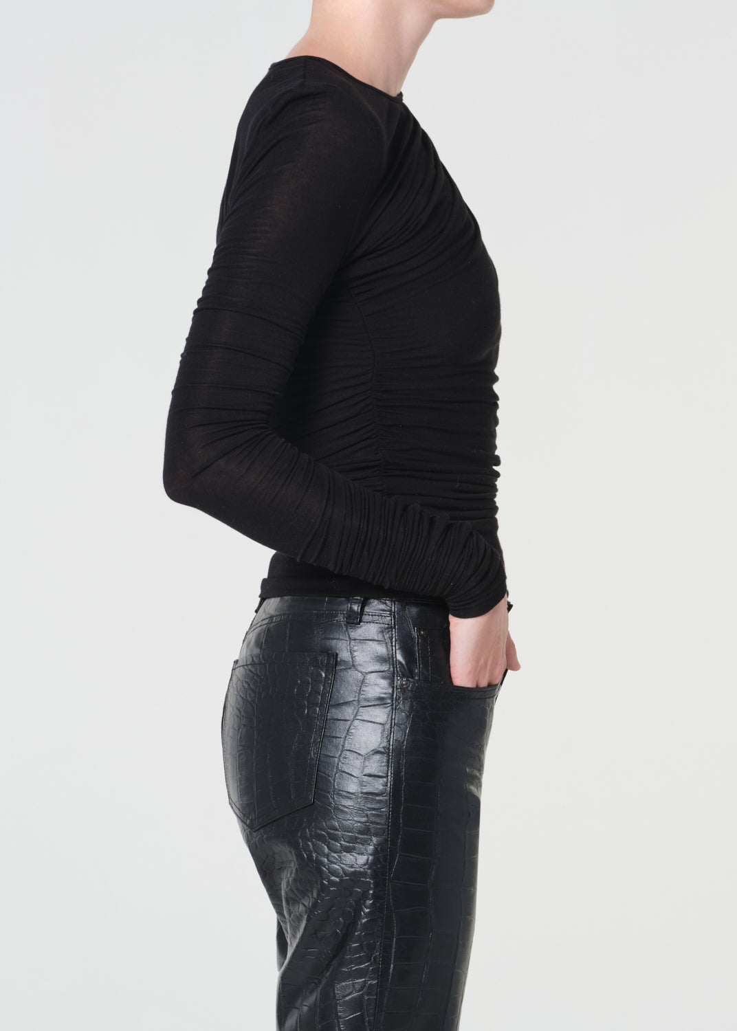 Person wearing a black ruched top and black leather pants on a light gray background