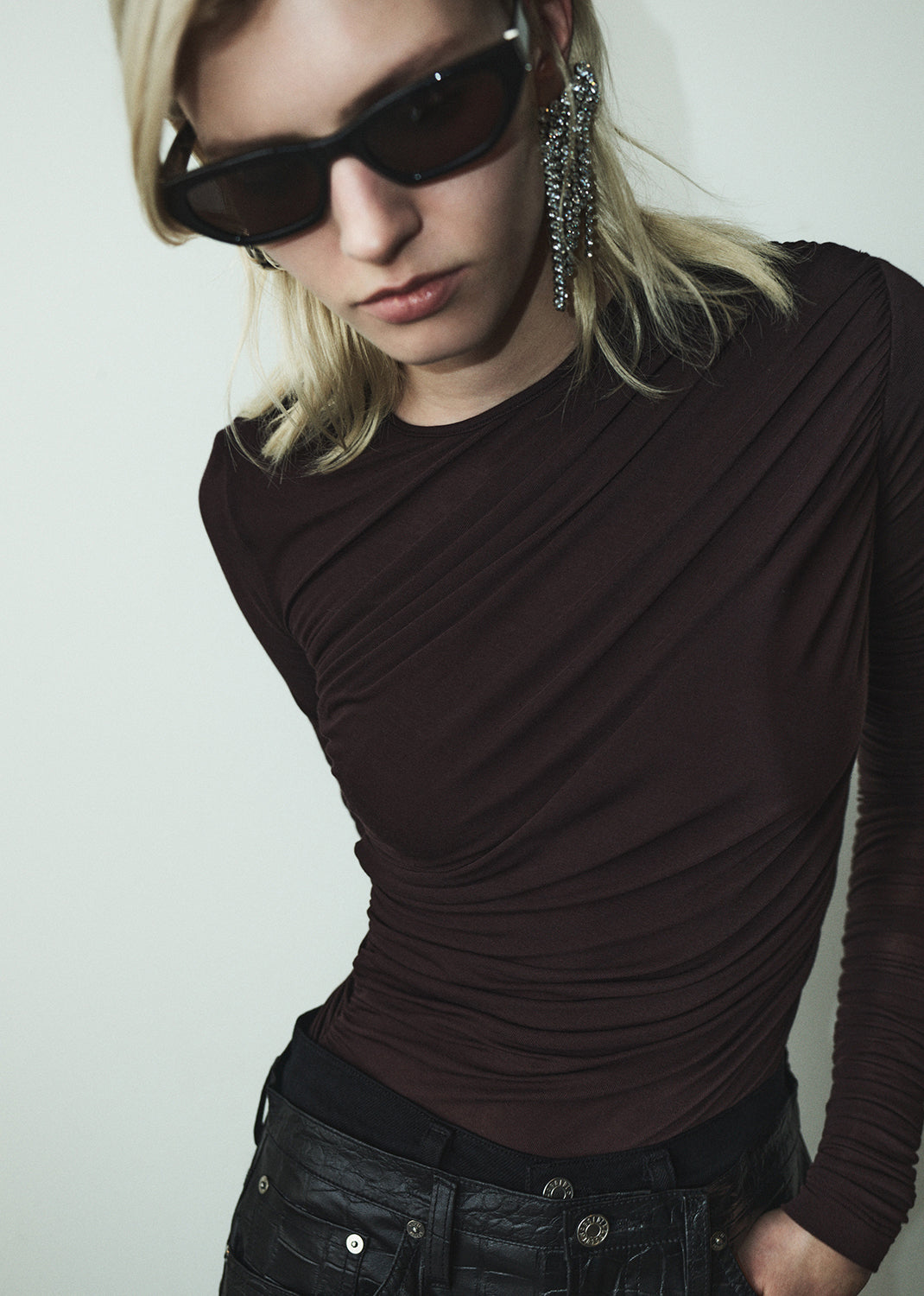Person wearing a dark brown top and sunglasses with a neutral background