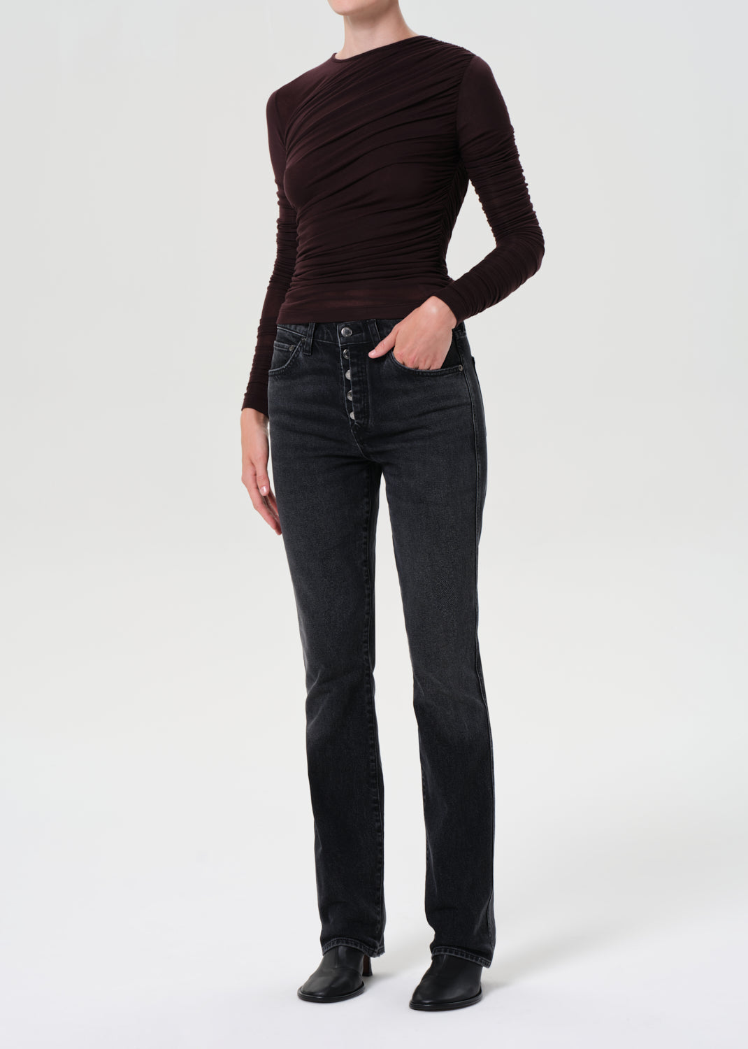 Person wearing a brown long-sleeve top and black jeans on a white background