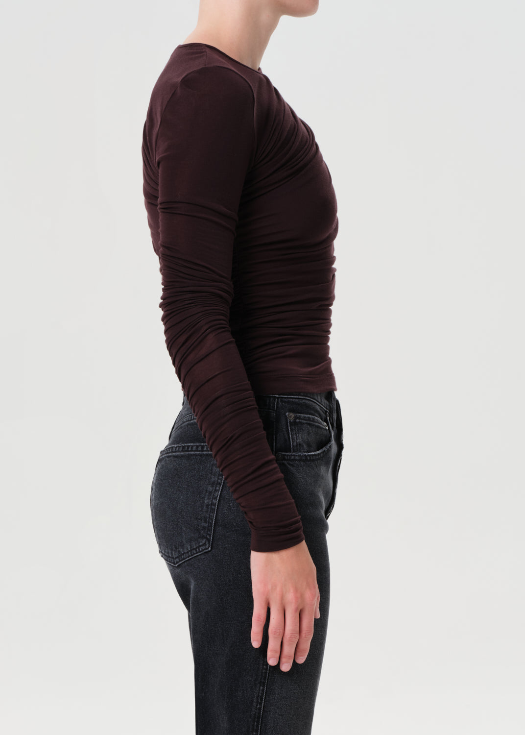 Person wearing a brown long-sleeve top and dark jeans on a light gray background