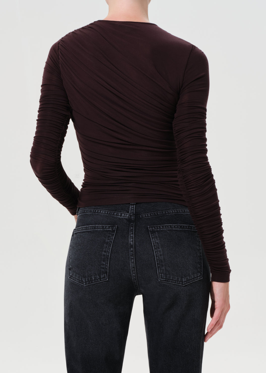 Person wearing a brown long-sleeve top and black jeans on a white background