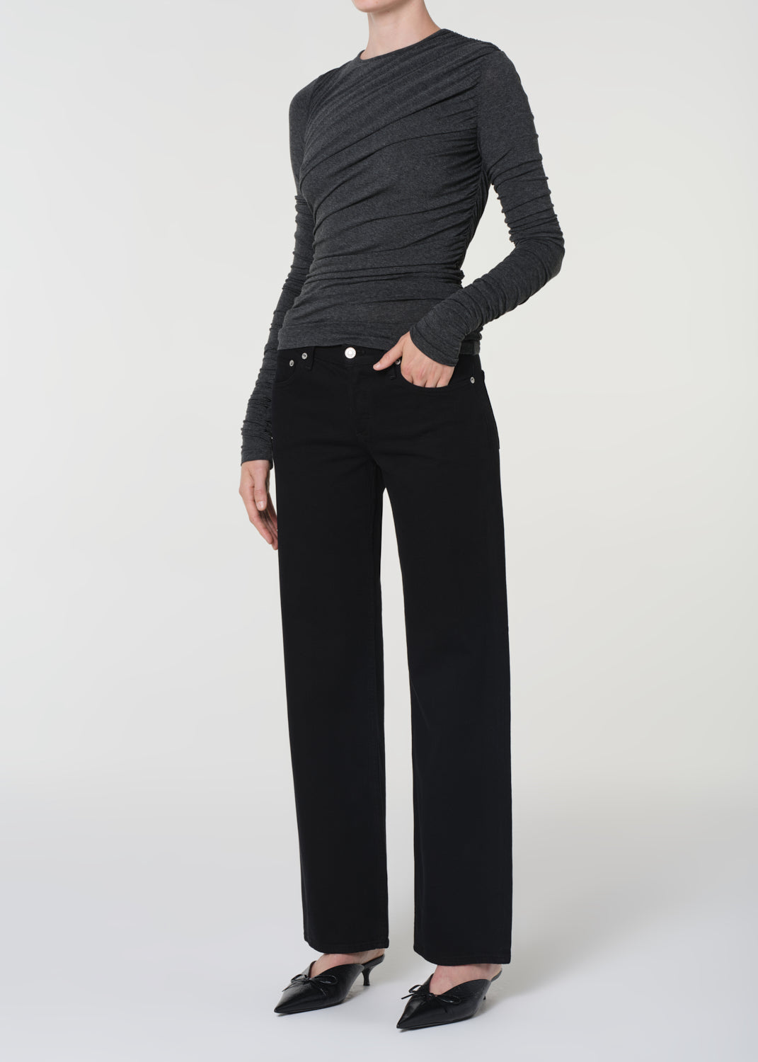 Person wearing a black ruched top and black pants on a white background
