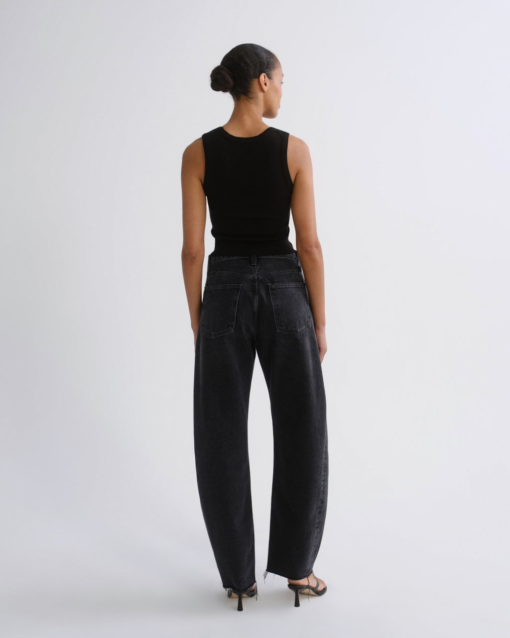 A model shown from the back wearing a black sleeveless top and wide-leg black jeans, standing against a plain light gray studio background.