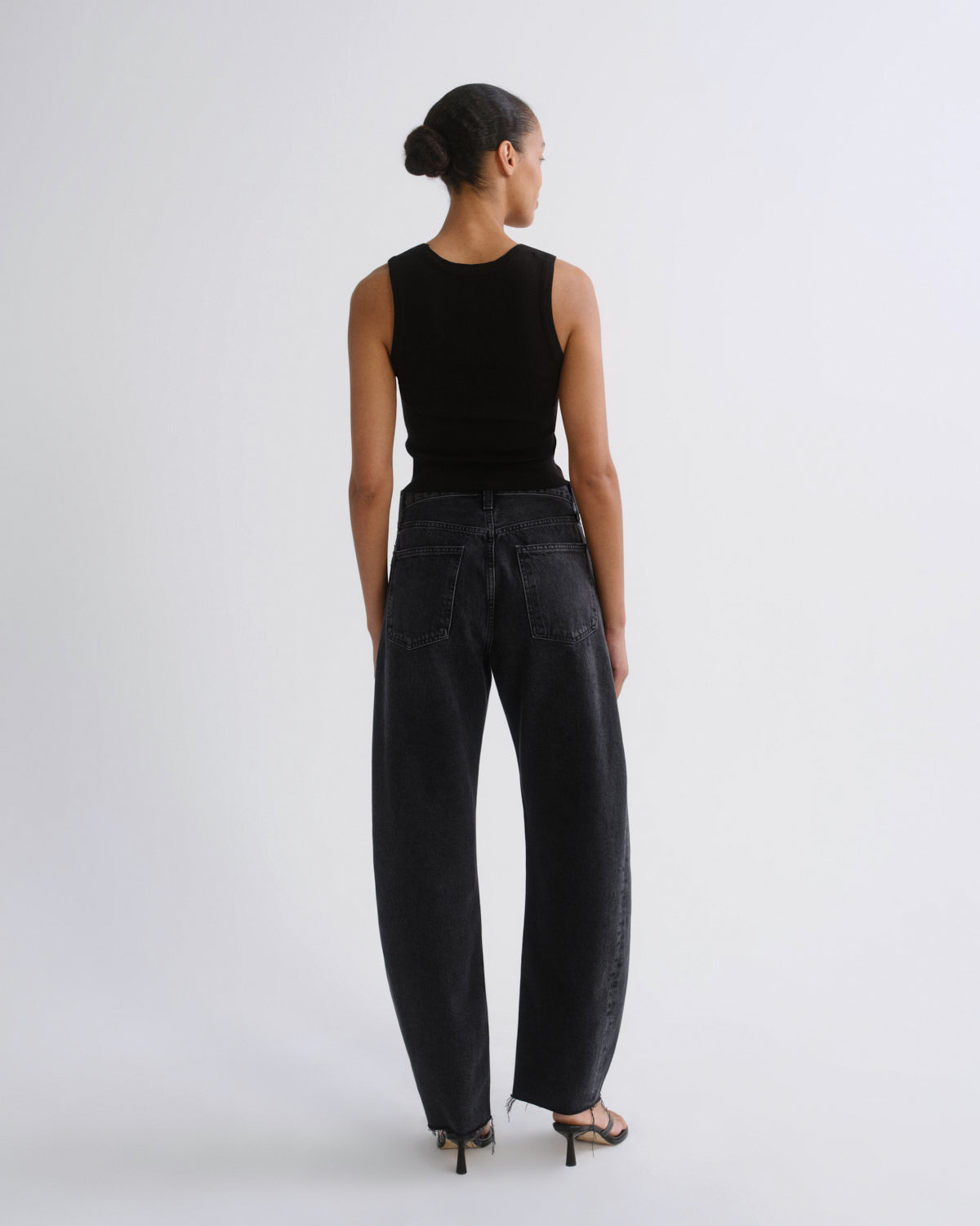 A model shown from the back wearing a black sleeveless top and wide-leg black jeans, standing against a plain light gray studio background.