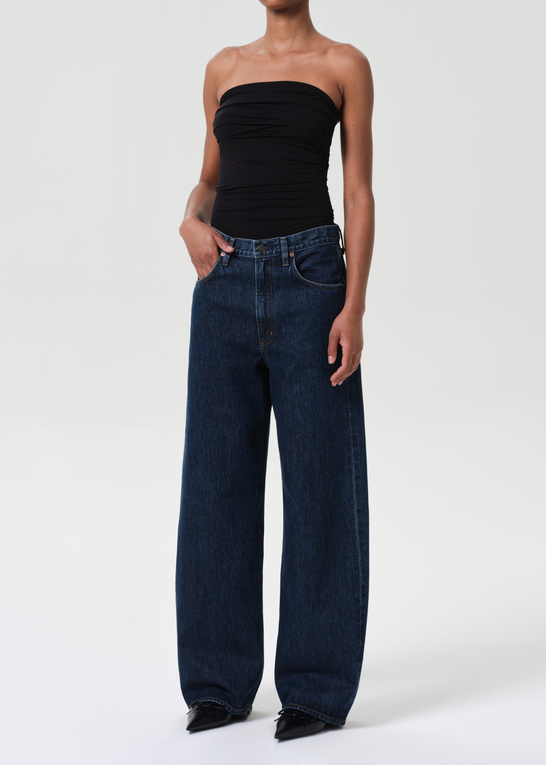 Person wearing a black strapless top and dark blue jeans on a white background
