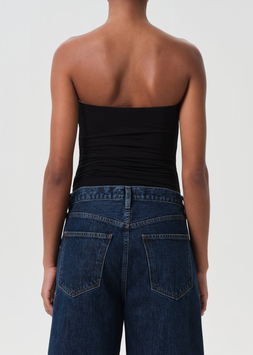 Person wearing a black strapless top and blue jeans on a white background