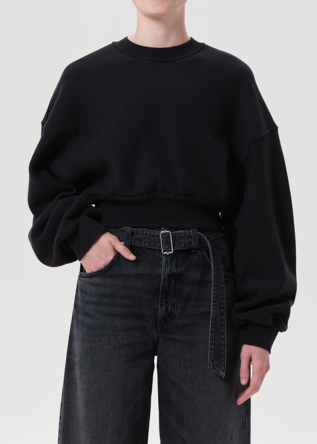 Person wearing a black oversized sweatshirt and black jeans on a white background