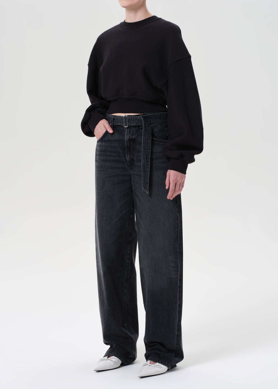 Person wearing a black sweater and dark jeans on a white background
