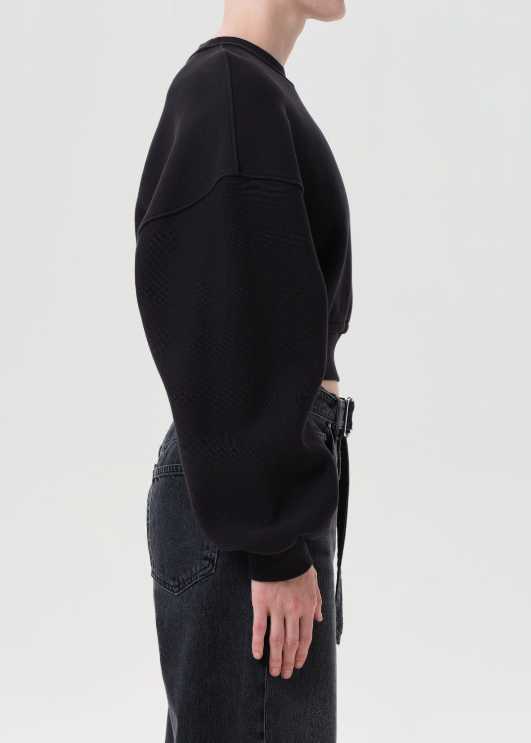 Person wearing a black sweatshirt and dark jeans on a light gray background