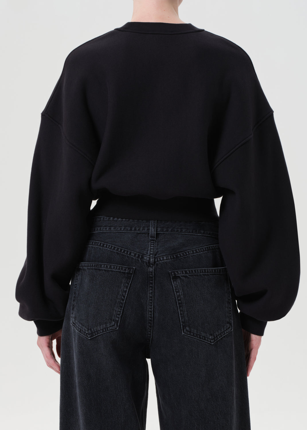Person wearing a black sweatshirt and dark jeans on a white background