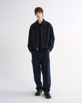 Person wearing a dark indigo denim jacket with matching dark indigo pants and black shoes on a grey background