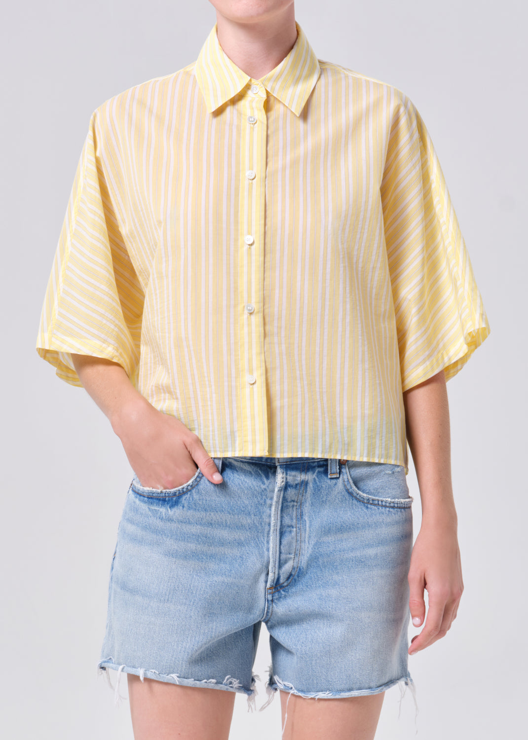 Person wearing a yellow striped shirt and denim shorts on a plain background