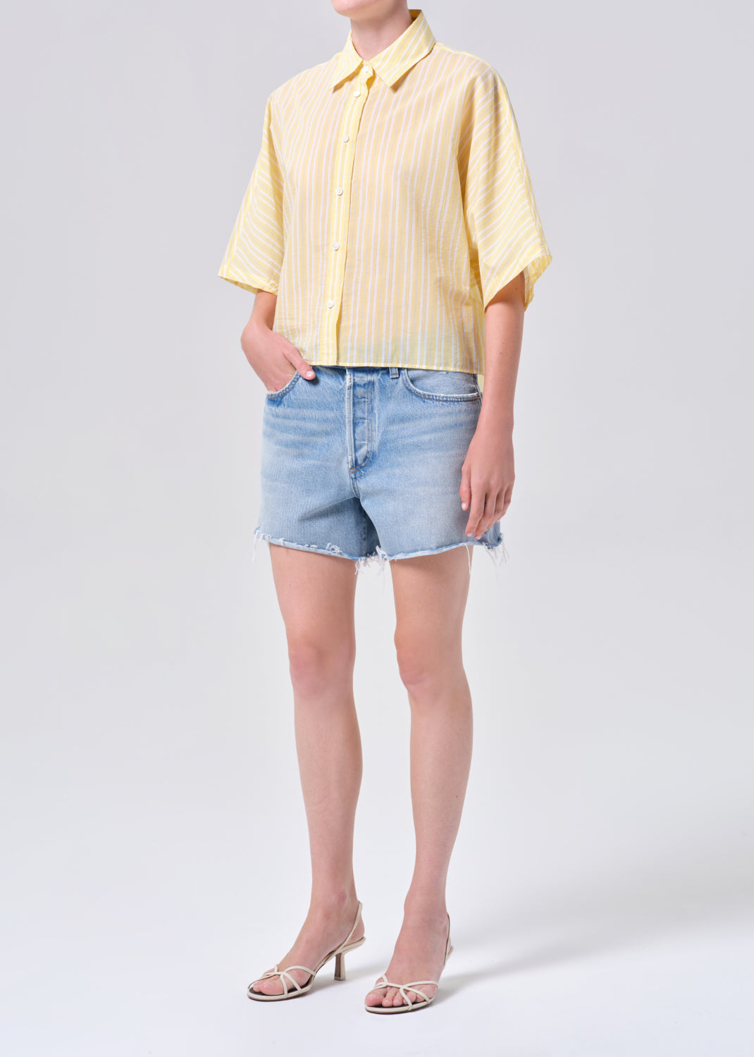 Person wearing a yellow striped shirt and denim shorts on a white background