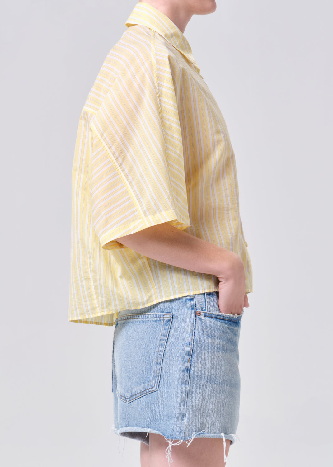 Person wearing a yellow striped shirt and denim shorts on a plain background