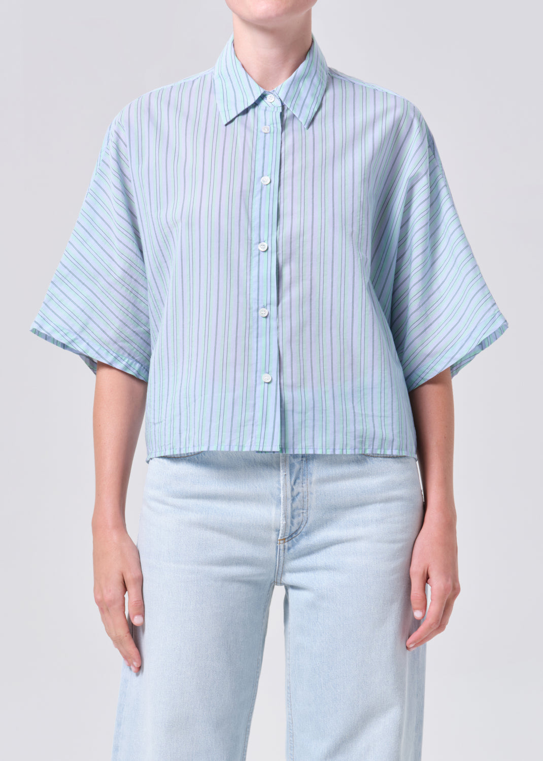 Person wearing a light blue striped shirt and light blue jeans on a plain background
