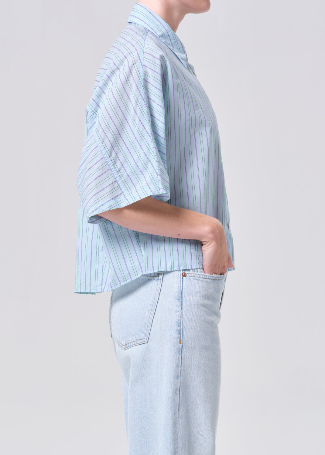 Person wearing a light blue striped shirt and light blue jeans on a plain background