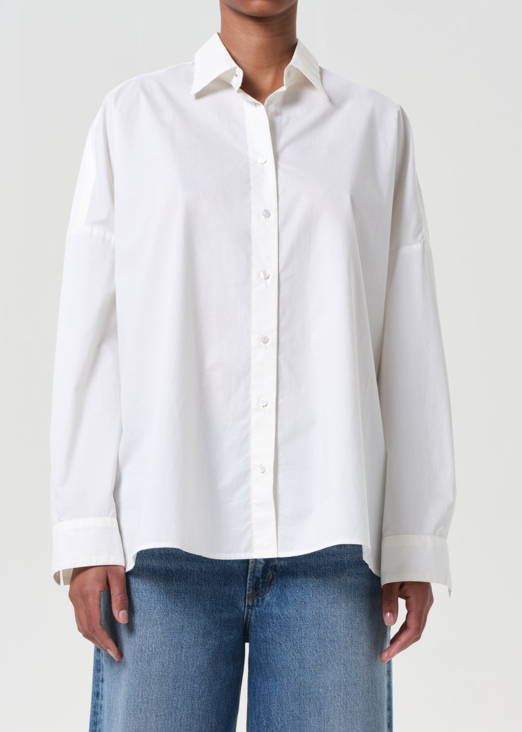 Person wearing a white button-up shirt and blue jeans on a plain background