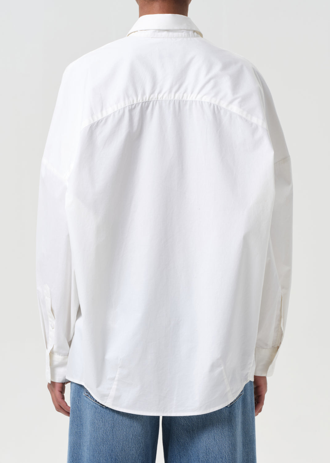 Person wearing a white shirt and blue jeans on a plain background