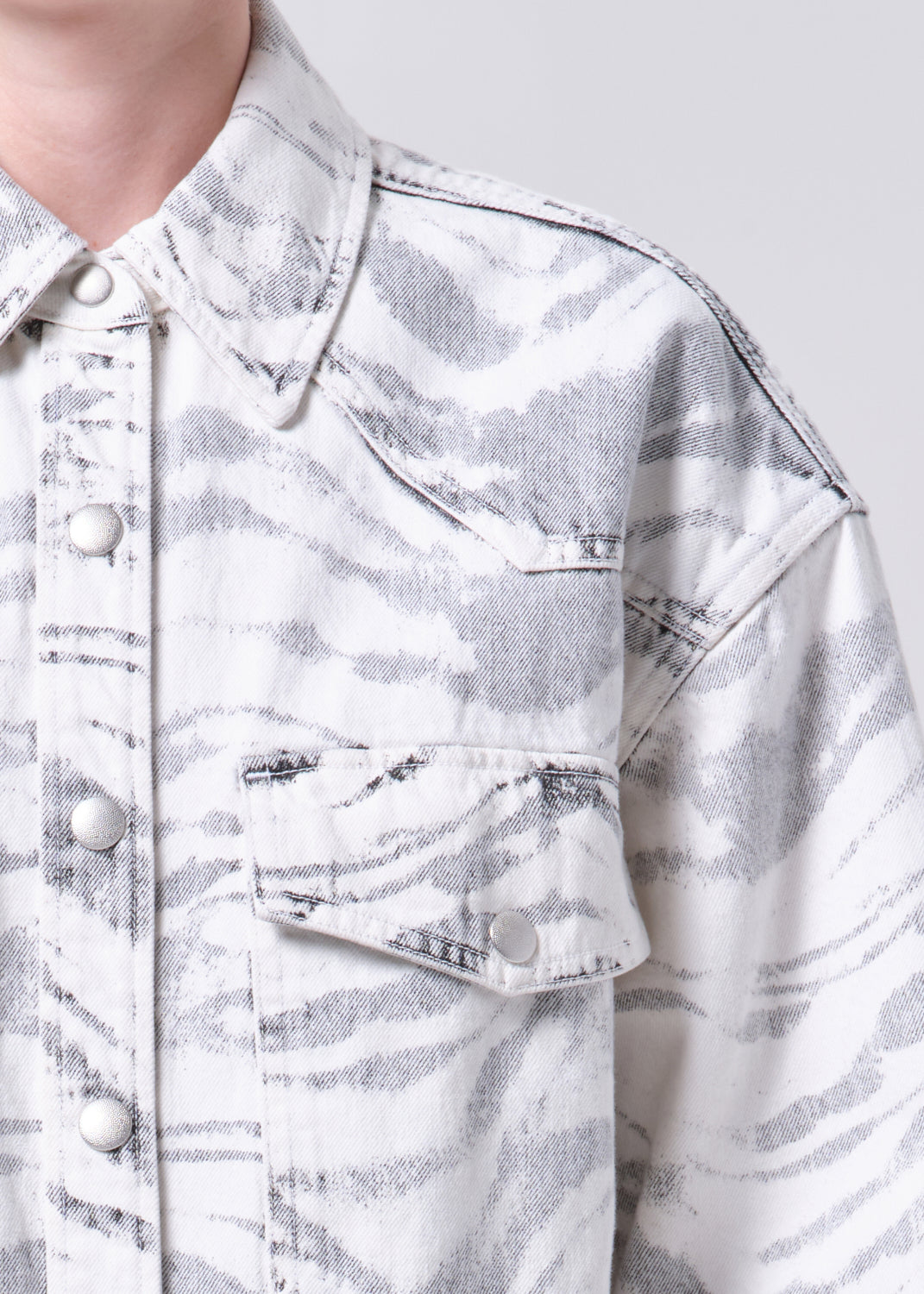 Close-up of a person wearing a light gray denim jacket with a subtle pattern.