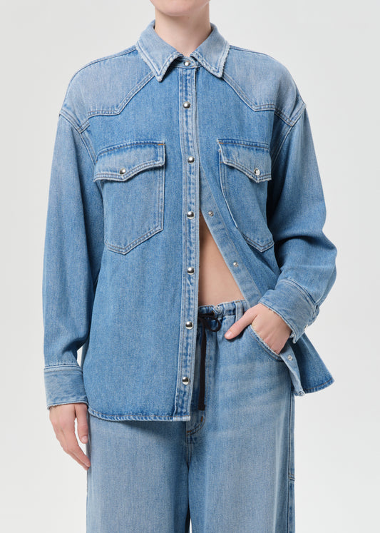 Person wearing a blue denim shirt and jeans on a light gray background