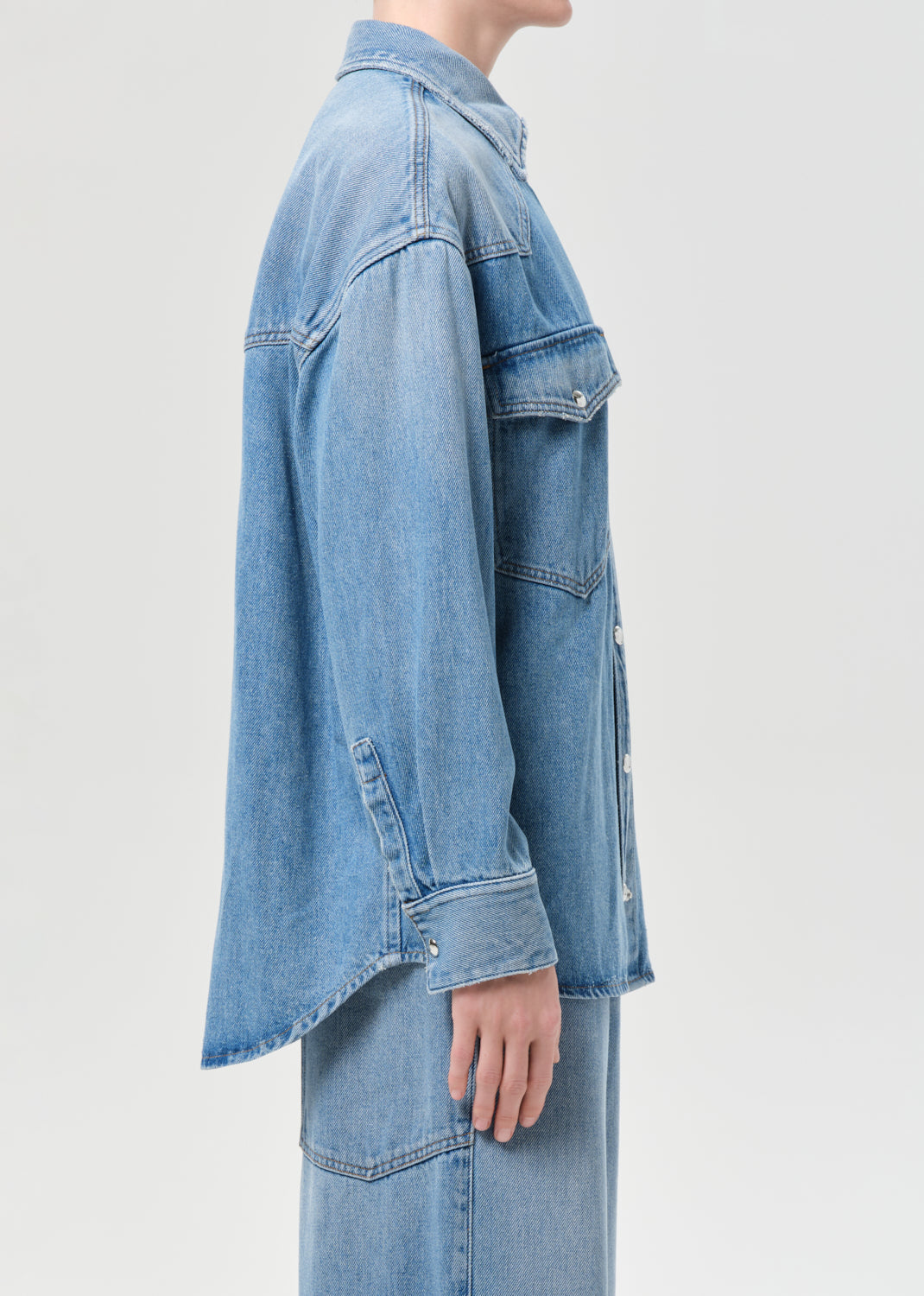 Person wearing a light blue denim jacket on a plain background