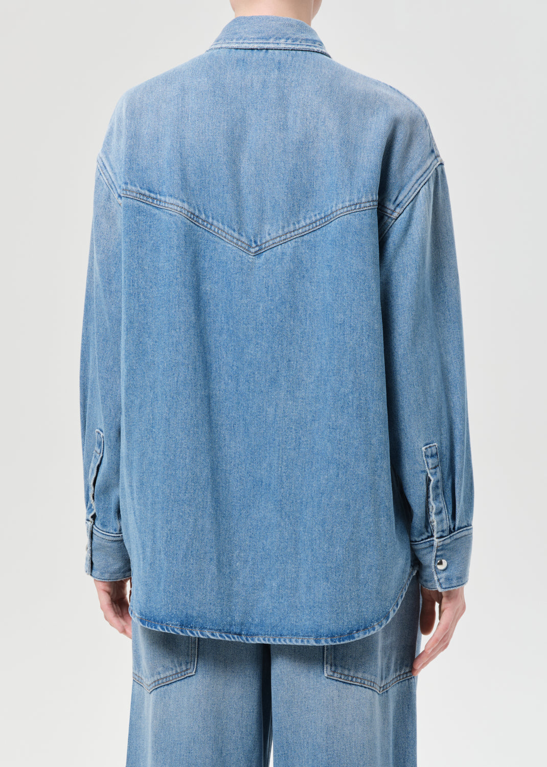 Blue denim shirt worn by a person on a light gray background