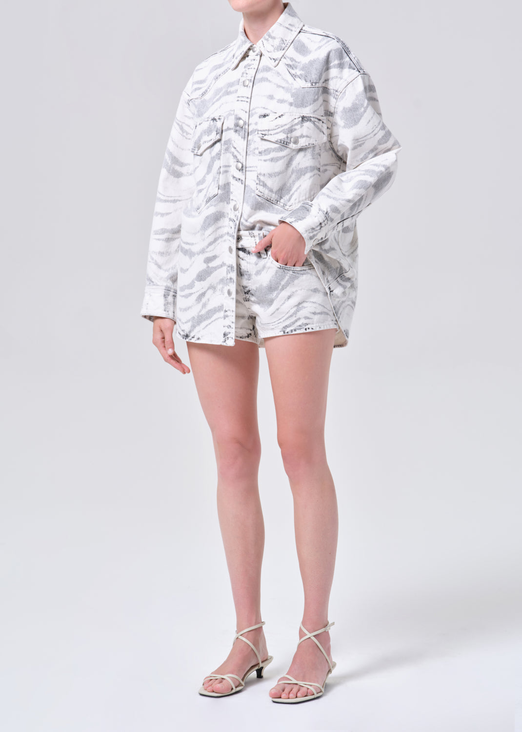 Person wearing a white patterned shirt and shorts on a light gray background