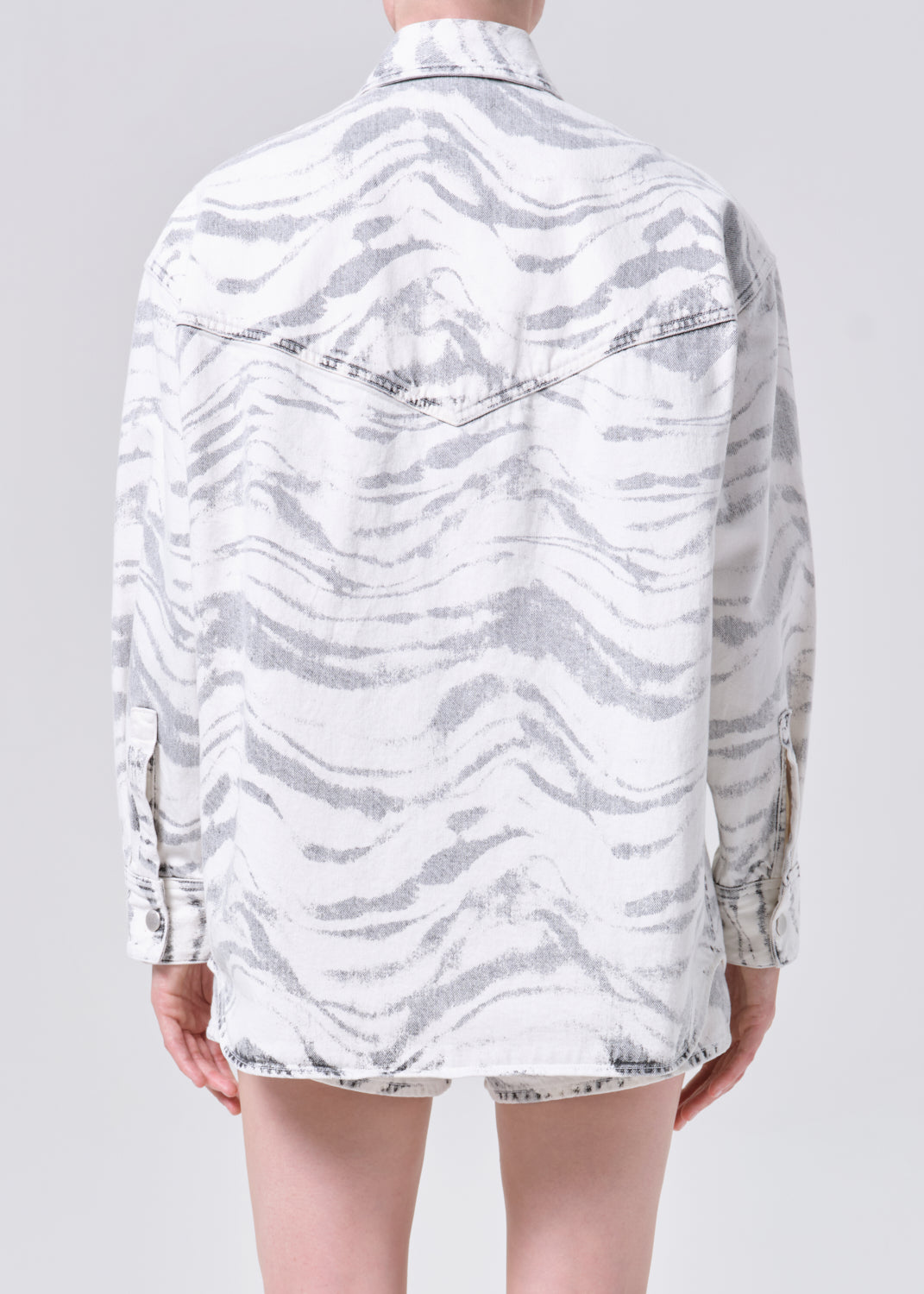 Person wearing a white and gray patterned shirt on a plain background