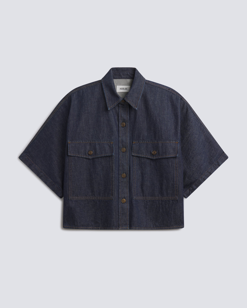 A dark indigo denim short-sleeve button-up shirt with two buttoned chest flap pockets, displayed flat against a light gray background.