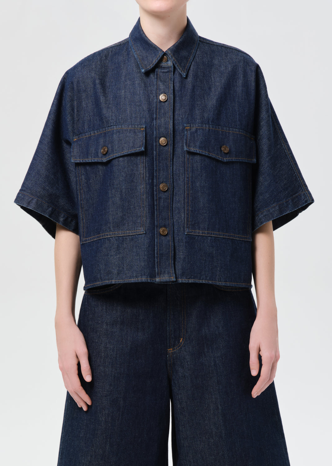 Person wearing a dark denim shirt with short sleeves on a white background