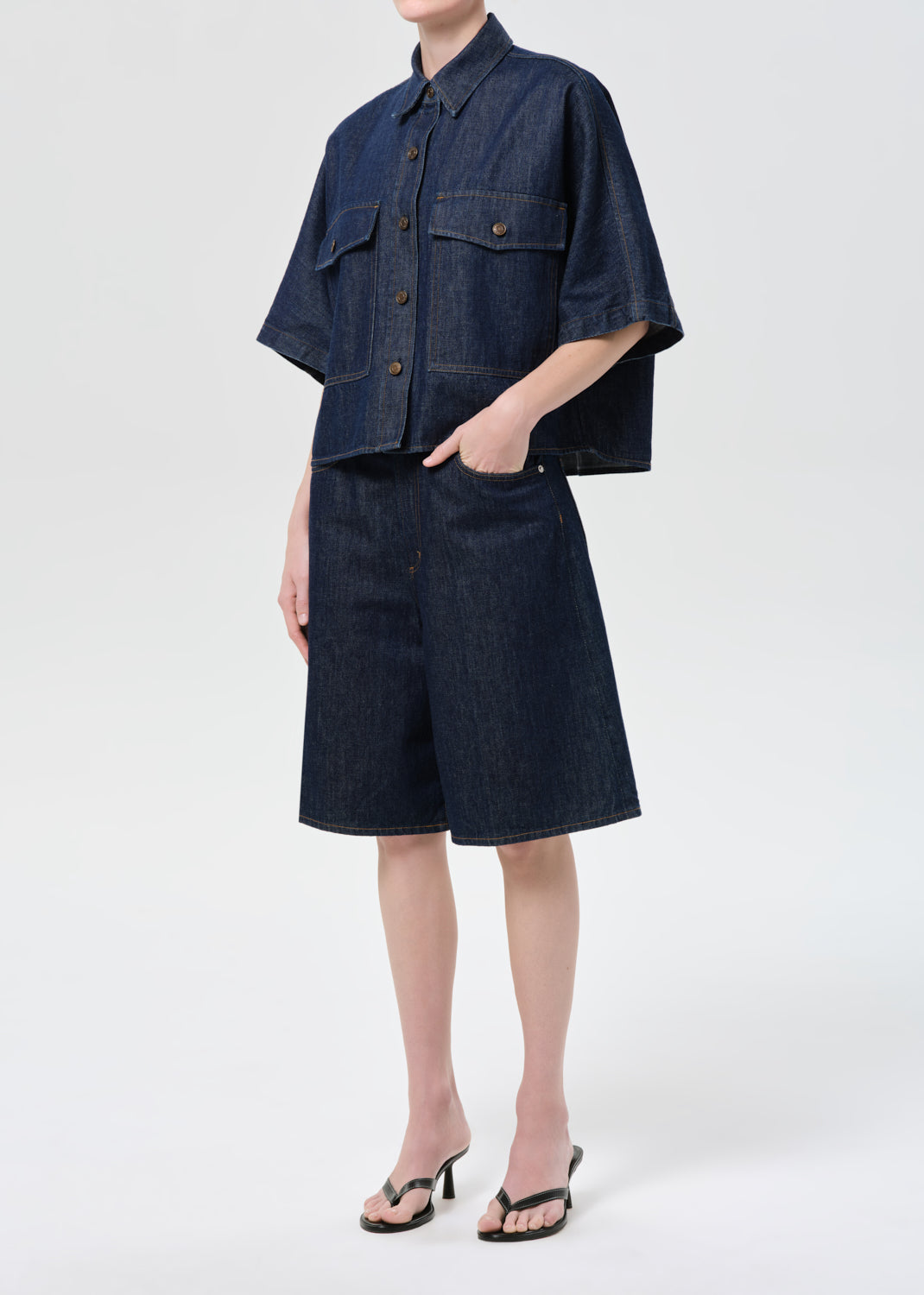 Person wearing a denim outfit with a shirt and shorts on a white background